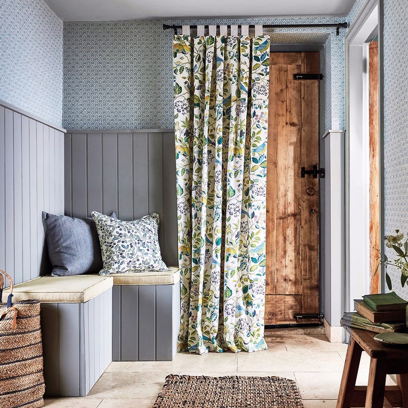 Hallway with patterned wallpaper, a wooden door, and a floral Birds & Berries curtain hanging from a black pole; matching fabric is on cushions.