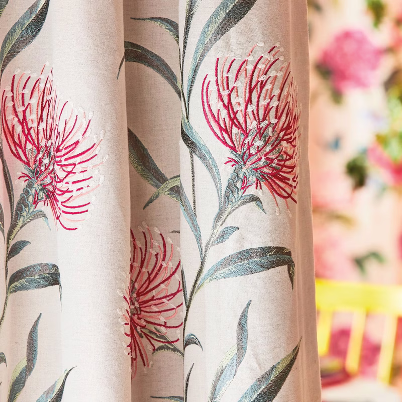 Close-up of patterned fabric made up as curtains in a room, with embroidered floral stems on pale cloth.
