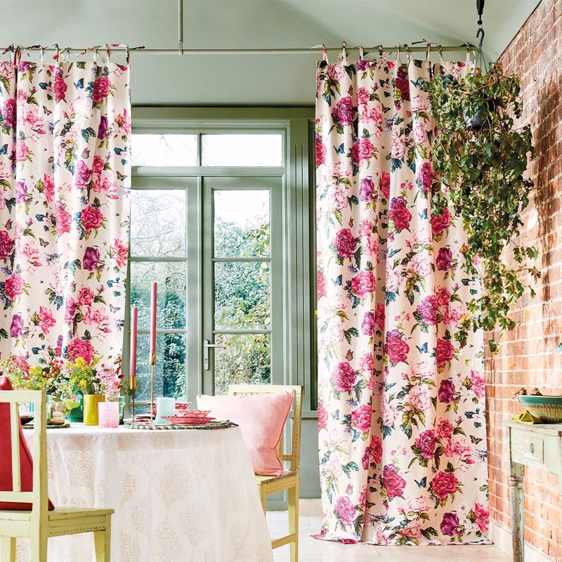 Dining room with floral fabric made up as curtains at a window and doorway, with a table and chairs in front.
