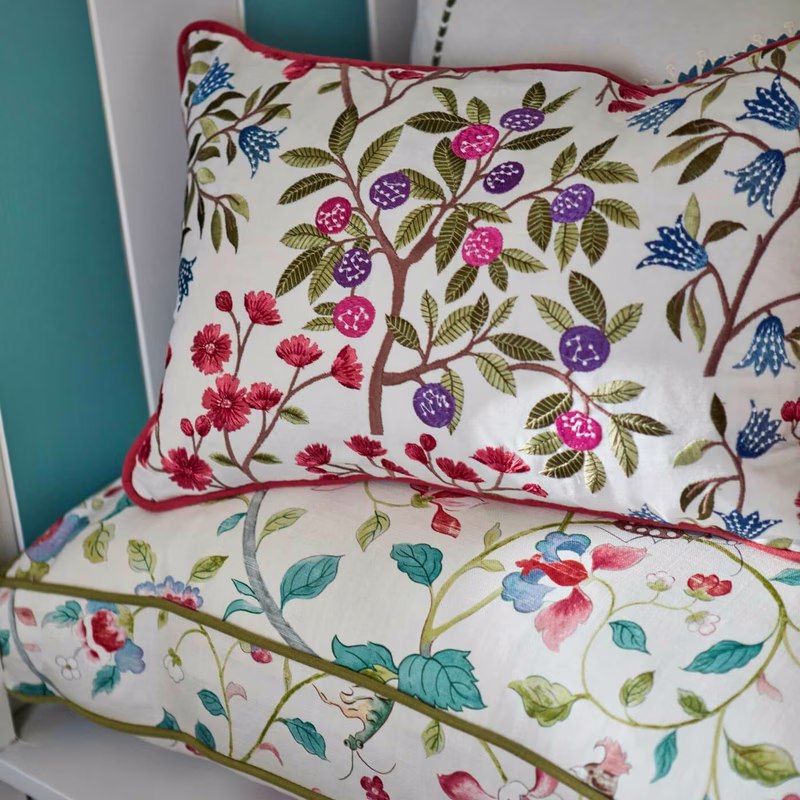 Patterned floral fabric shown made up as a piped cushion and a bench cushion in a room.