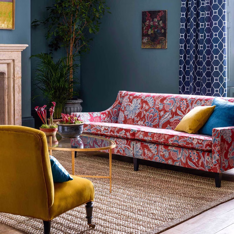 Living room with a red patterned sofa upholstered in Shalimar fabric, alongside a blue patterned curtain and a mustard chair.