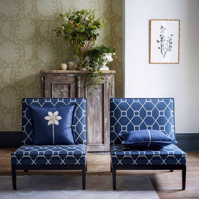 A room with two blue patterned upholstered chairs and matching cushions in front of a decorative wall and cabinet.