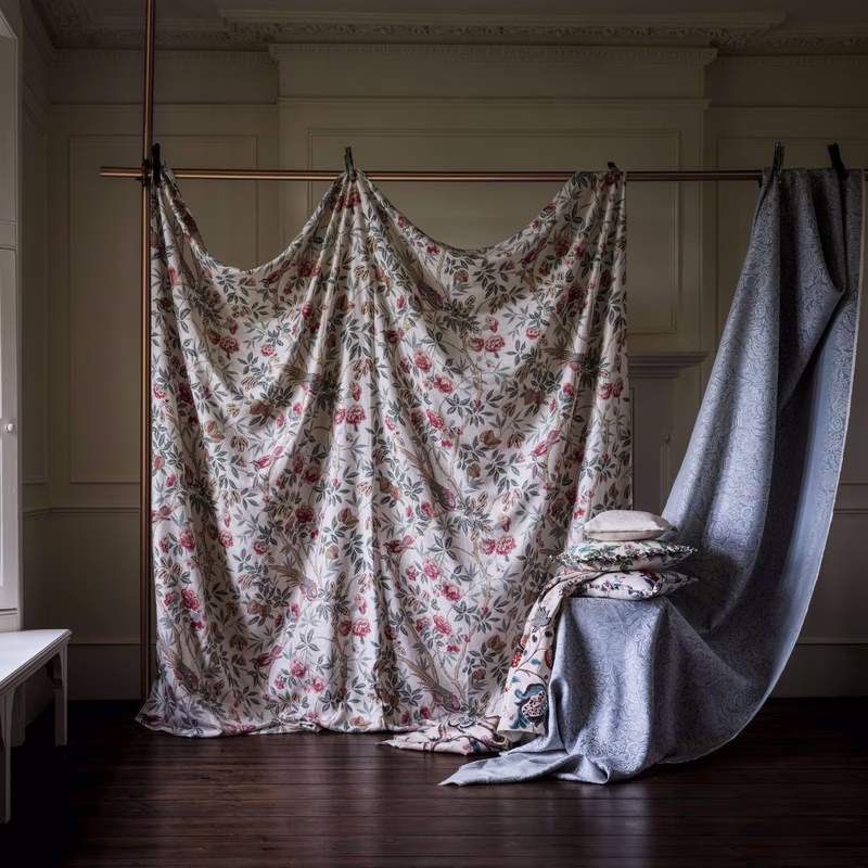 Room setting with two lengths of fabric hung from a pole, one floral cloth draped as curtains and one blue patterned cloth draped with cushions on a stool.