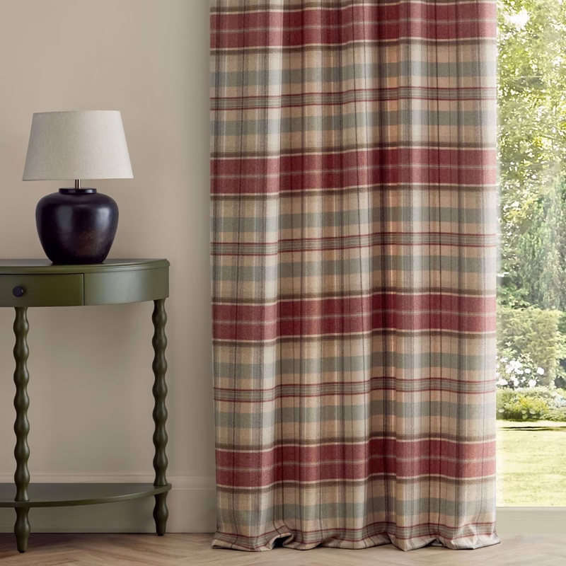 A room with plaid fabric made up as curtains beside a side table and lamp.