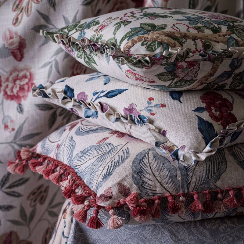 Stacked floral-pattern cushions in a room, made up as cushions with ruffled piping and tassel trim.