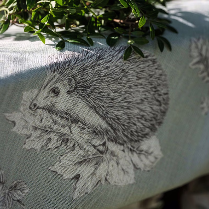 Close-up of a patterned upholstered cushion or seat with a hedgehog design and trailing leaves in a room.