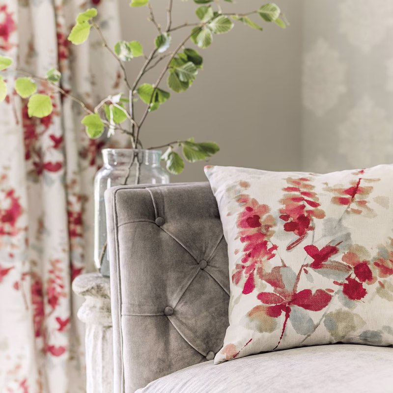 Grey upholstered chair with a floral cushion, with matching patterned curtains in the background.