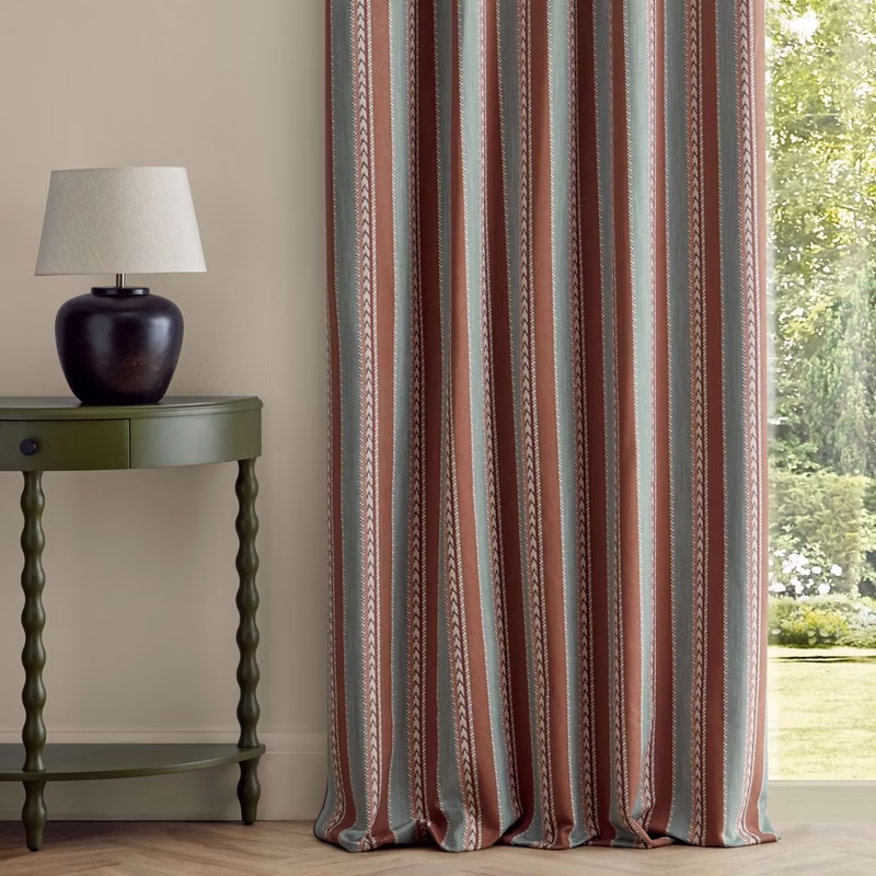 A room with a side table and lamp beside striped patterned curtains hanging to the floor.