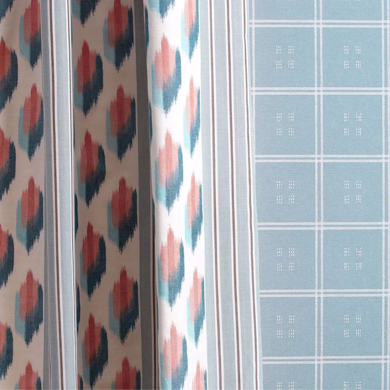 A fabric sample book with several patterned textiles laid flat, showing ikat-style designs and a pale checked pattern.