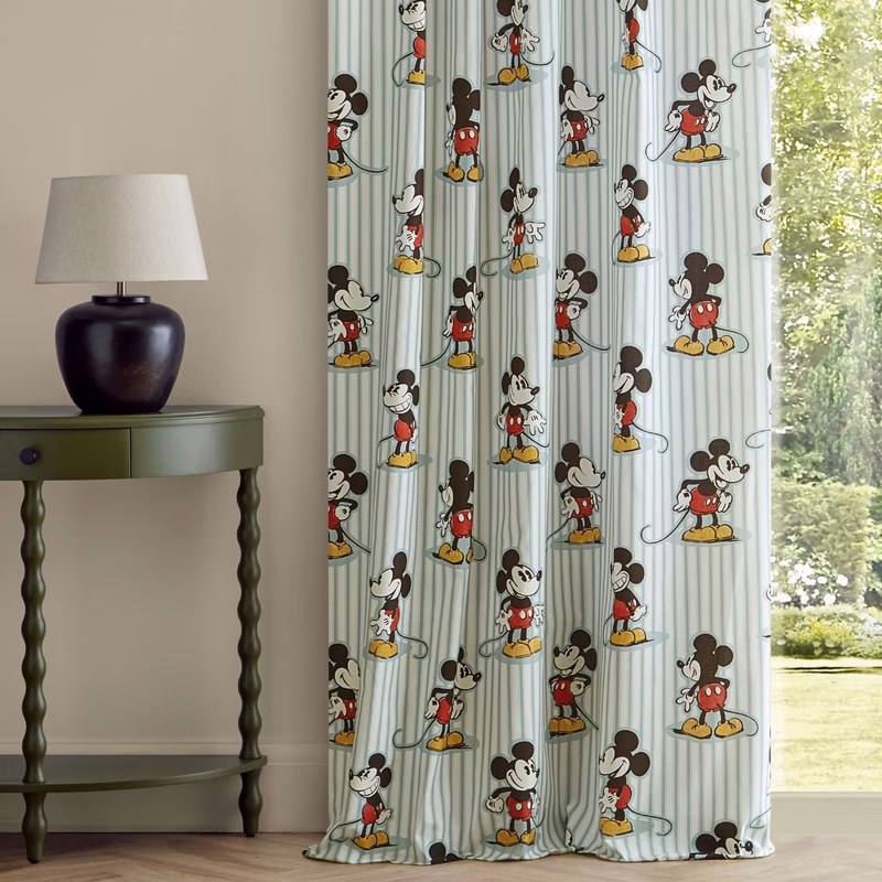 A room with a side table and lamp beside full-length Mickey Stripe curtains hanging to the floor.