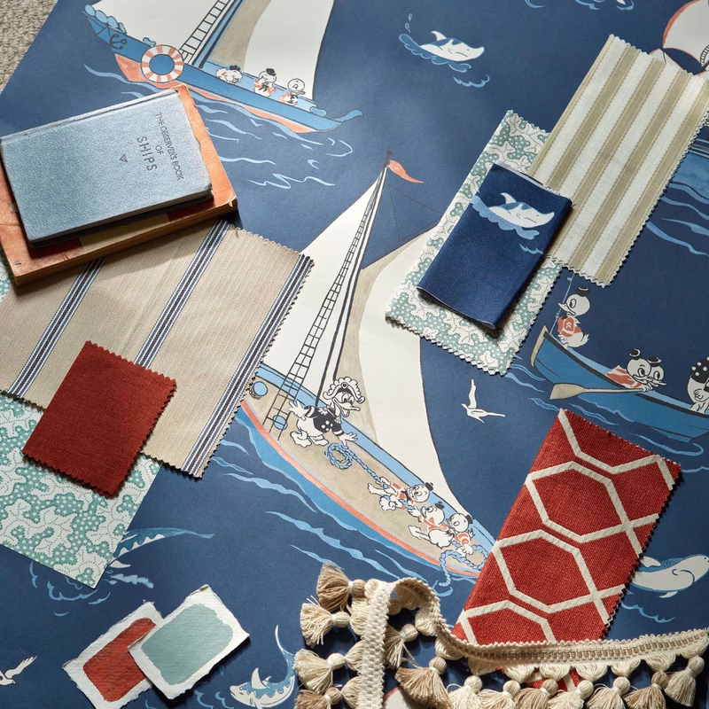 Showroom flat lay of a nautical Disney fabric design with sample swatches, trimmings and a pair of books laid on the cloth.
