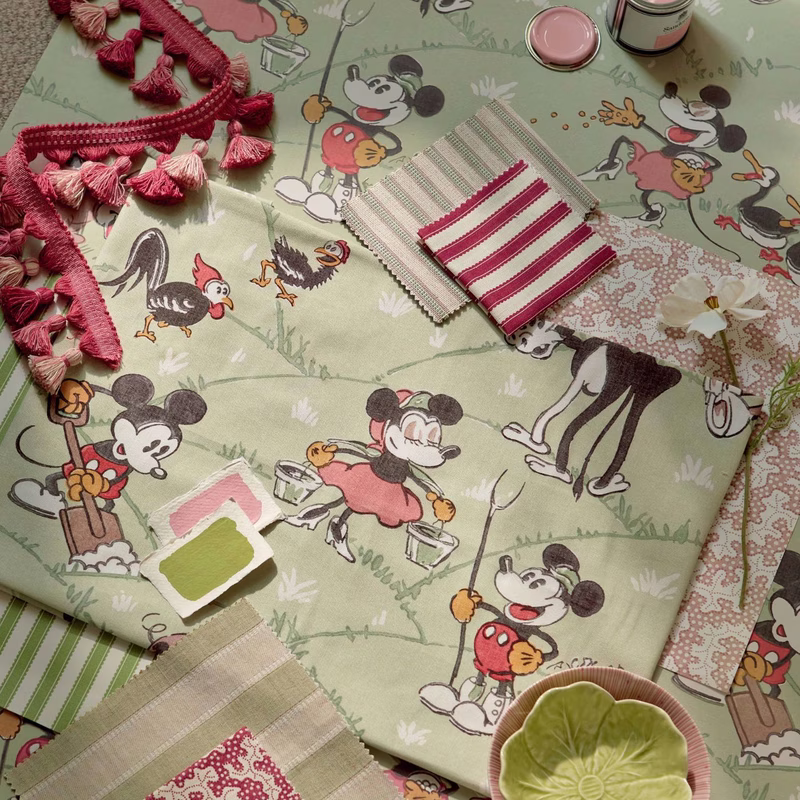 Studio photograph of the Mickey At the Farm fabric laid flat with swatches and trims on top, showing a printed cotton cloth.