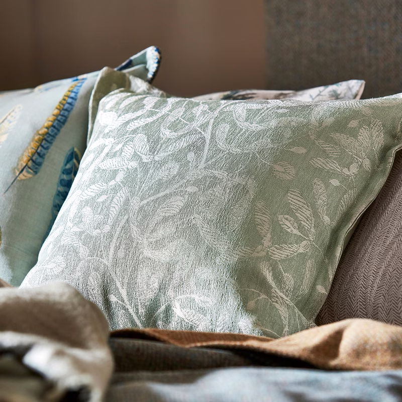 Cushions on a sofa, including a pale green leaf-patterned cushion made in the fabric and a blue cushion with embroidered trim.