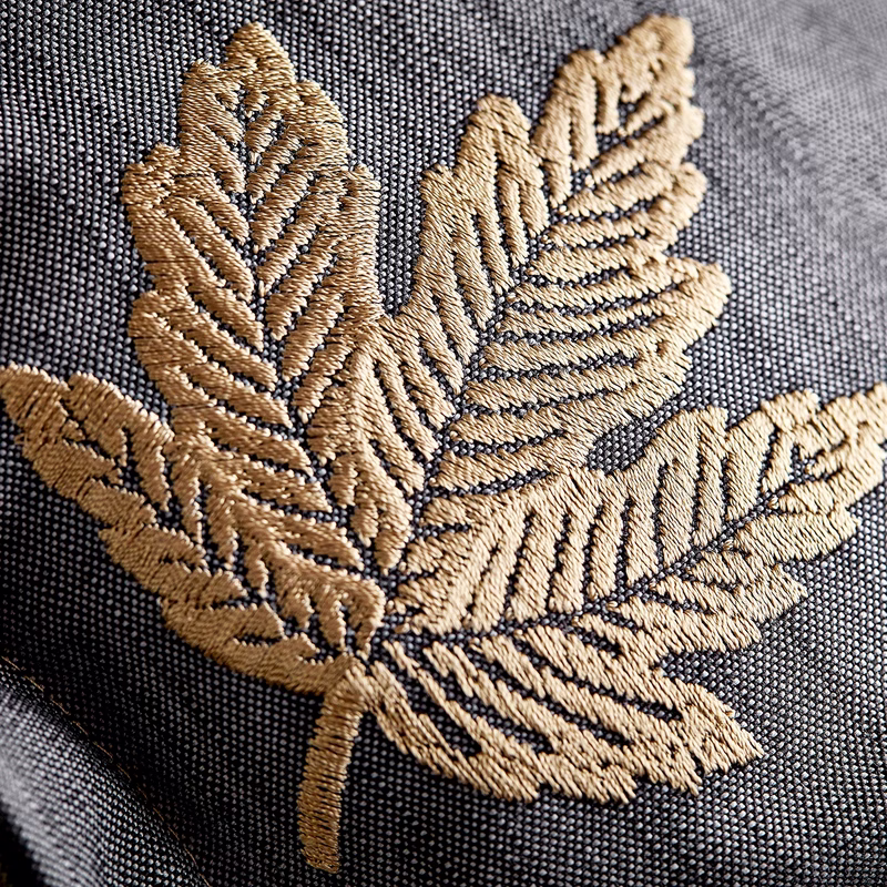 Close-up of dark woven upholstery fabric with a gold embroidered leaf motif, made up as upholstery.
