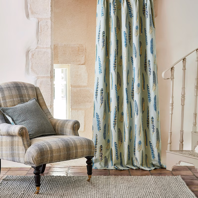 Living room with a plaid armchair and a feather-patterned curtain hanging to the floor beside a staircase.