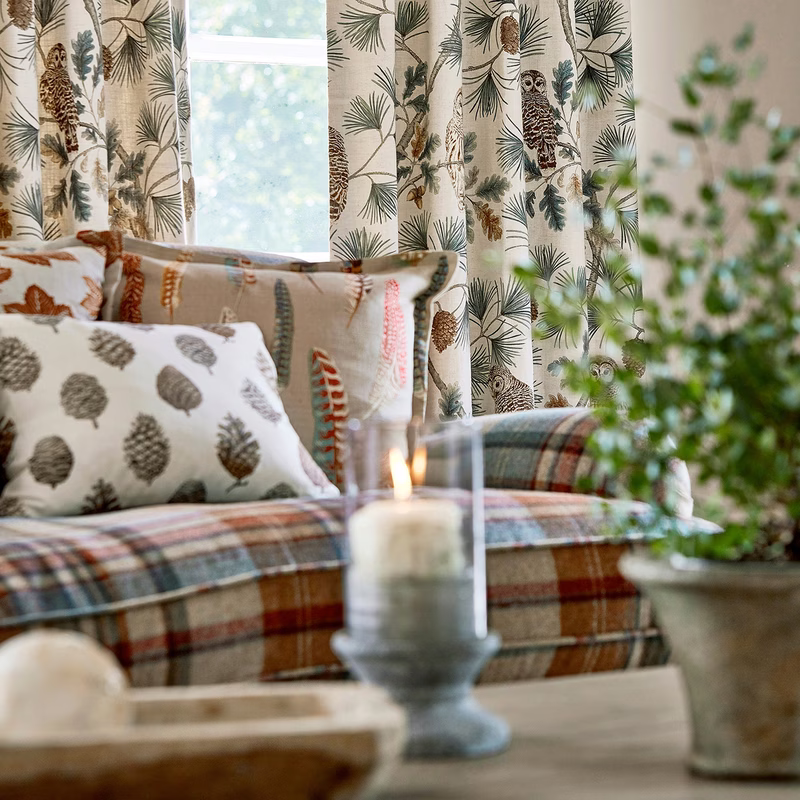 Sitting room with Owlswick fabric made up as curtains and cushions, shown with a plaid-upholstered sofa and patterned cushions.