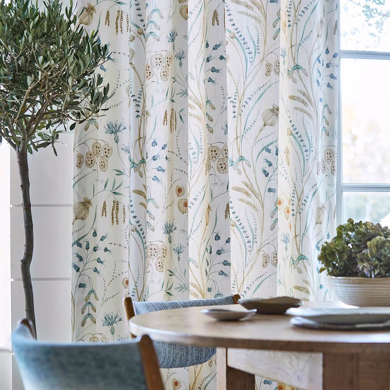 Dining room with botanical patterned fabric made up as curtains at the window.