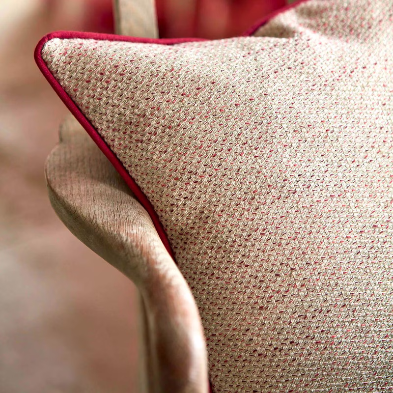A close-up of a chair upholstered in textured cream and pink woven fabric with dark pink piping.