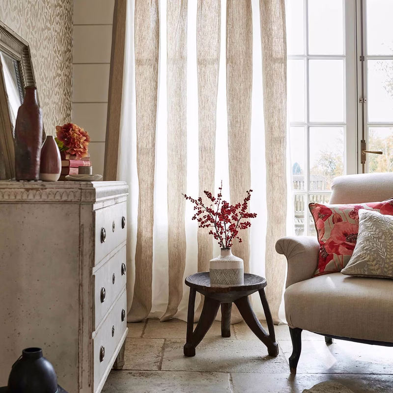 A sitting room with tall striped curtains framing a window, with a sofa and patterned cushions nearby.
