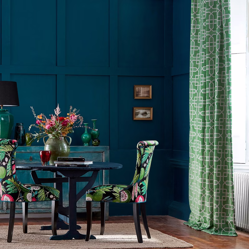 Dining room with a green geometric curtain at the window and patterned upholstery on chairs.