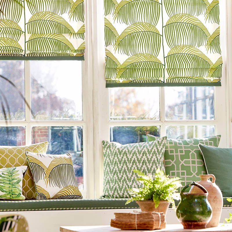 Bright room with windows, roman blinds and cushions upholstered in a green leaf print fabric.