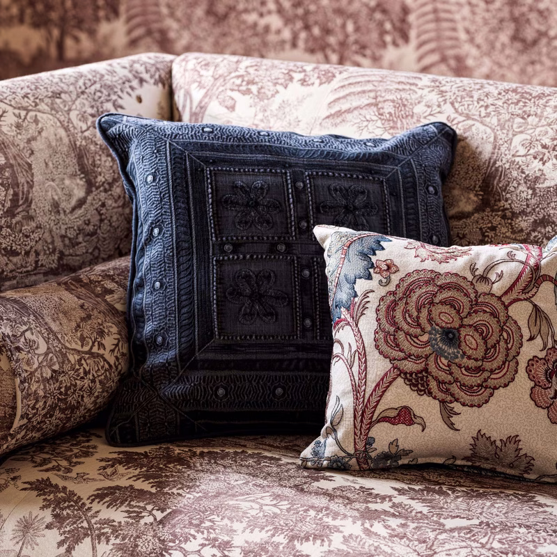 A sofa upholstered in toile fabric with matching patterned cushions, including a dark blue stitched cushion and a floral cushion.
