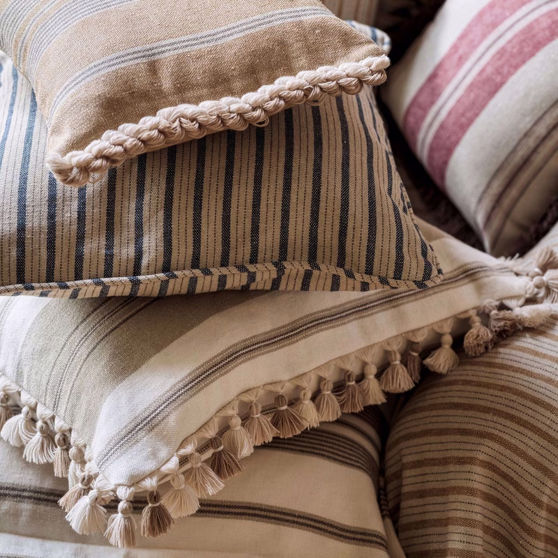 Stacked striped cushions in a room, trimmed with tassels and braid edging.