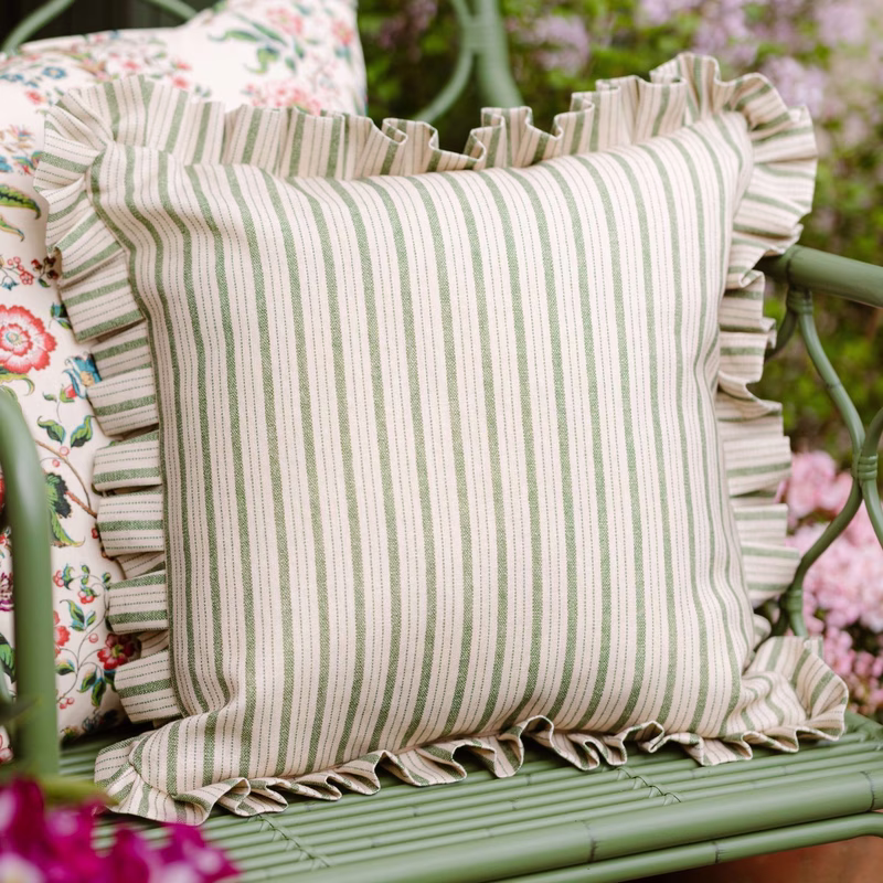 A striped cushion with frilled edges on a green garden chair, with another floral cushion partly visible behind it.
