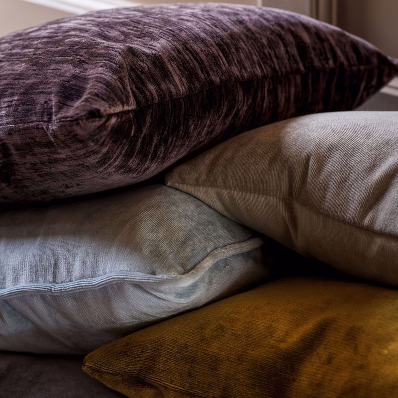 Stack of velvet cushions in a room, showing the fabric made up as cushions.