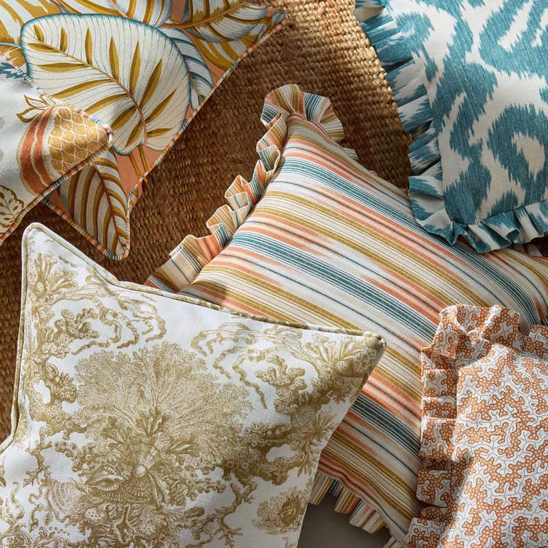 Several patterned cushions made up with frilled edges are arranged on a woven surface, including striped and floral prints.