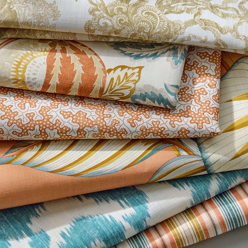 Stacked folded fabric samples of Sanderson’s Calathea print in a workshop display, showing several overlapping lengths of cloth with different leaf and stripe patterns.