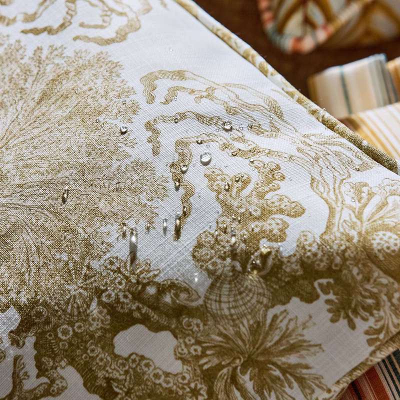 Close-up of a patterned outdoor fabric on a cushion, with water droplets on the surface.