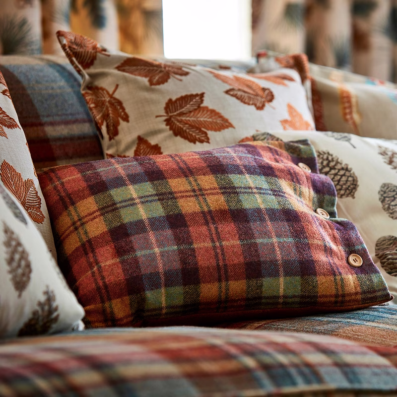 A close-up of patterned cushions on a sofa, featuring a tartan-check cushion with button detail and leaf-print cushions behind it.