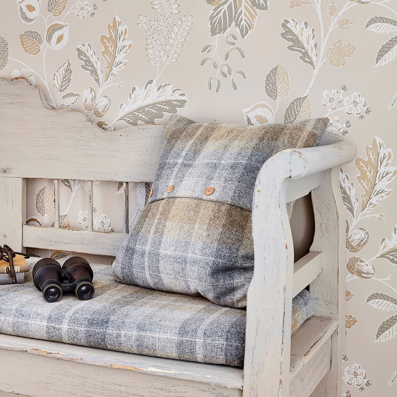 A rustic white wooden bench in a patterned room is upholstered in checked fabric and has a matching cushion.