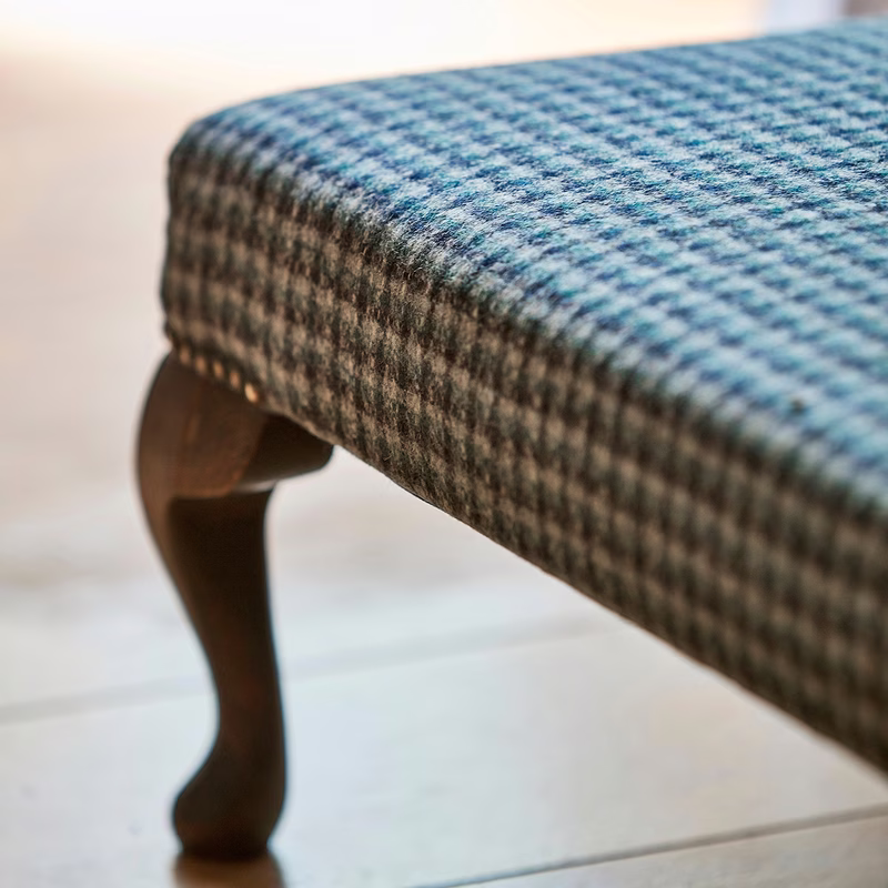 Close-up of a padded stool upholstered in a blue and grey check fabric, with a wooden leg visible.