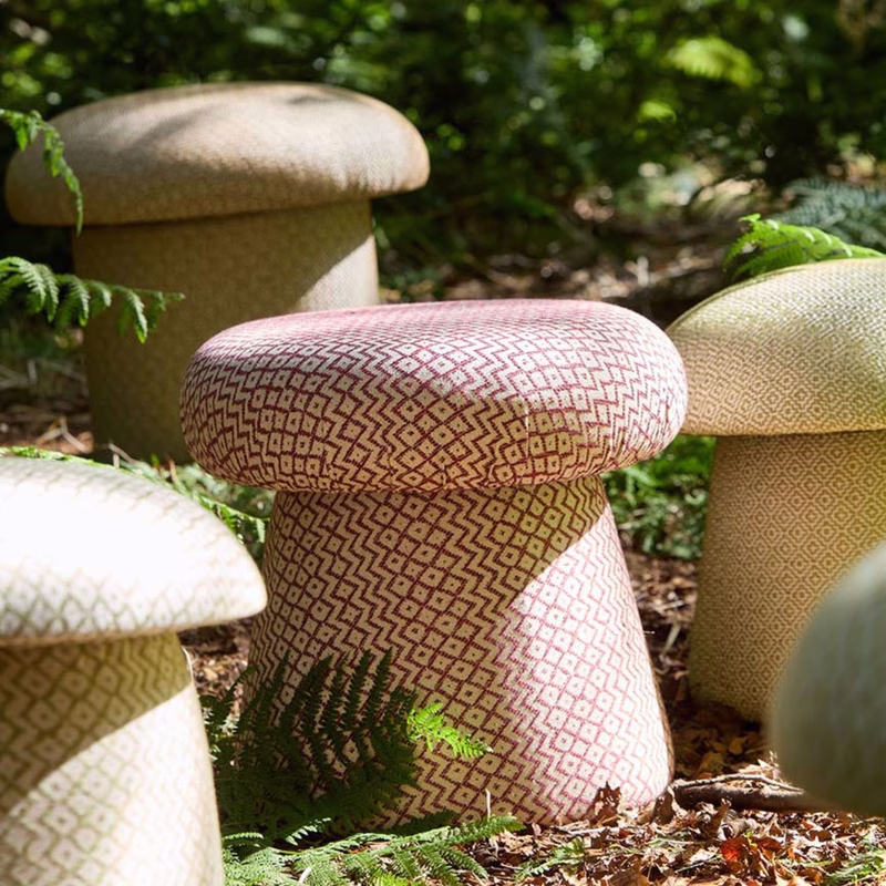 Five mushroom-shaped stools upholstered in patterned fabric are arranged in a leafy garden setting.