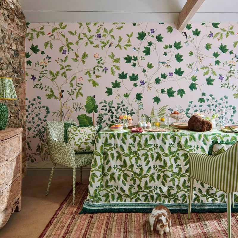 Dining room with botanical wallpaper and chairs, showing the fabric as a tablecloth over the table and as upholstery on the chairs.