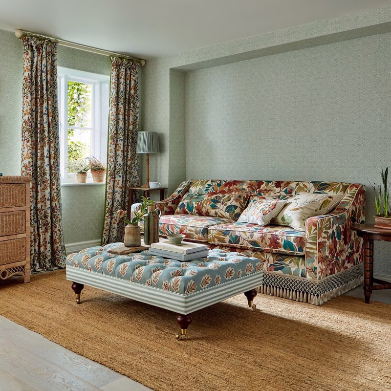 Living room with patterned curtains and a floral upholstered sofa and ottoman in the Sessile Leaf fabric.