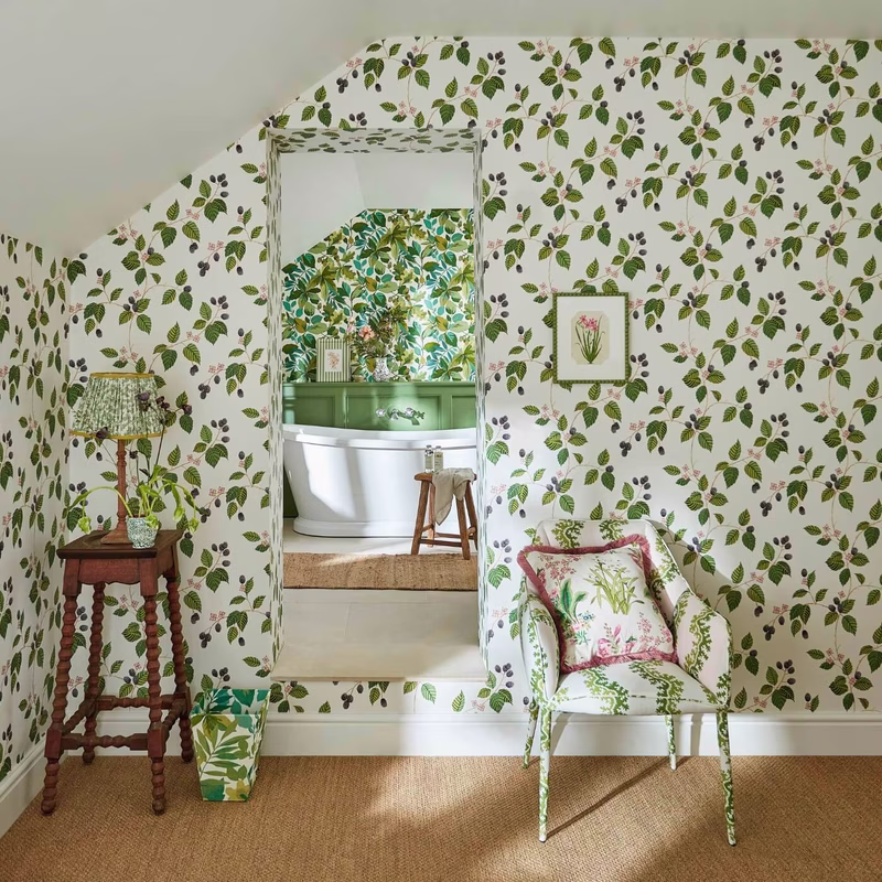 A patterned bedroom-like room with the Oxbow print used on the wallpaper and on an upholstered chair and cushion.