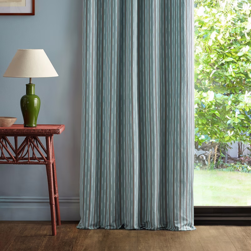 Striped fabric hangs as full-length curtains in a room beside a table and lamp.