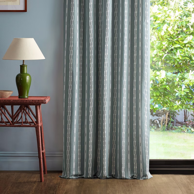 Living room with striped fabric hung as full-length curtains beside a window, pooling slightly on the floor.
