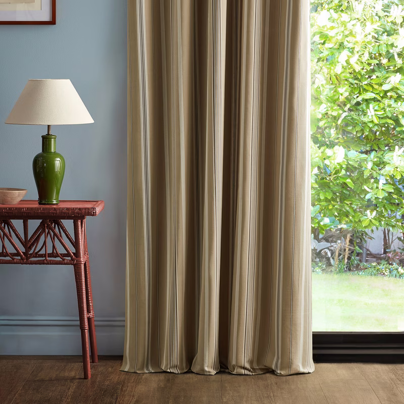 A living room with a striped curtain hanging full length beside a window, with a lamp on a table nearby.