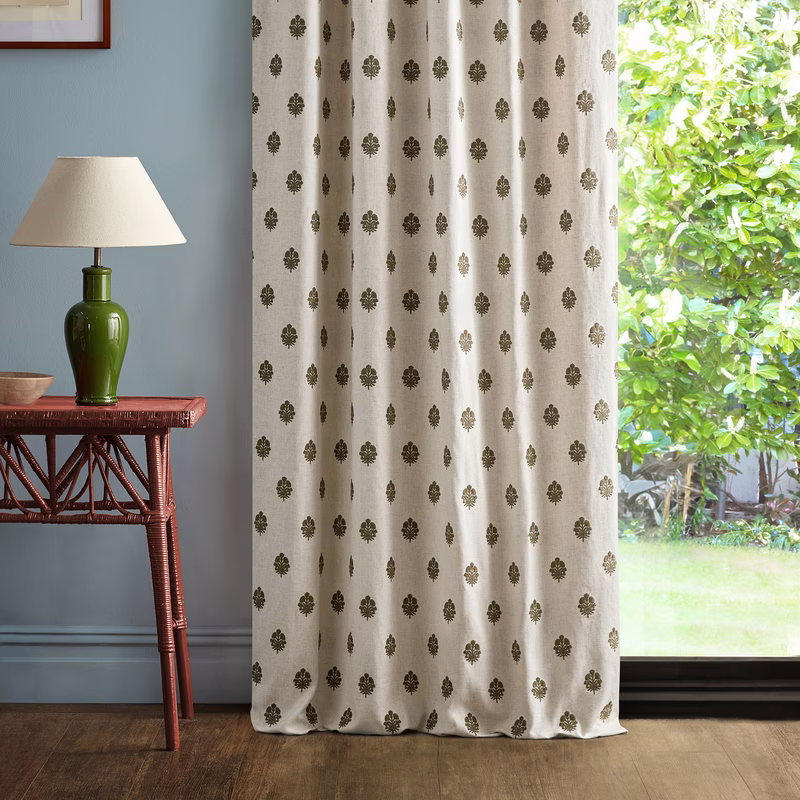 A room with a small table and lamp beside patterned fabric made up as full-length curtains hanging in front of a window.