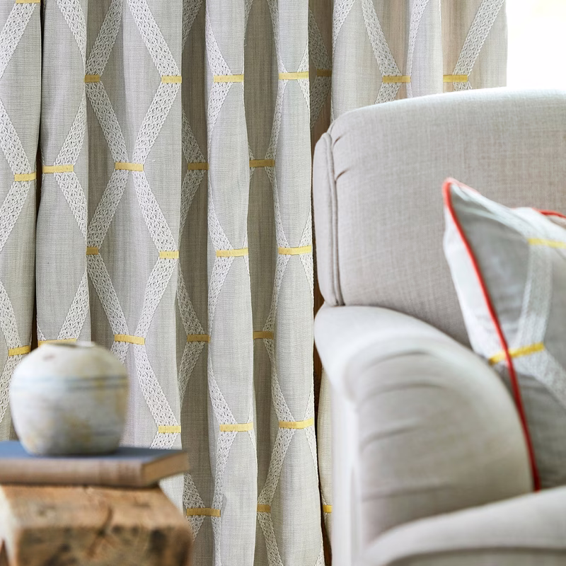 Sitting room with Hemsby fabric made up as curtains behind a pale armchair with a matching cushion.