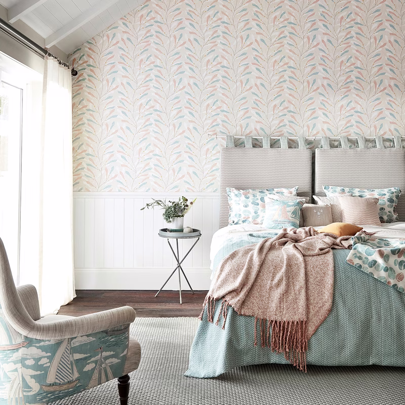 Bedroom with Sea Kelp wallpaper and a matching upholstered bed and chair, plus a bedspread and cushions made up in the fabric.