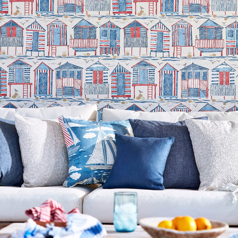A sofa with matching scatter cushions sits against beach-hut patterned wallpaper in a living room.
