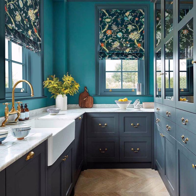 Teal-painted kitchen with Roslyn patterned fabric made up as Roman blinds at the windows.