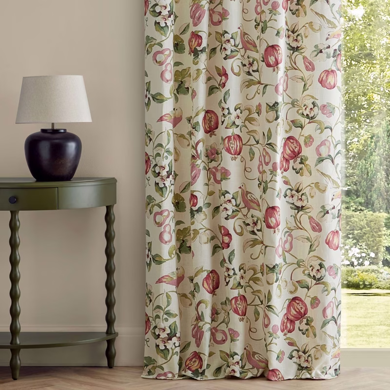 A floral printed curtain hangs by a window beside a green side table and lamp.