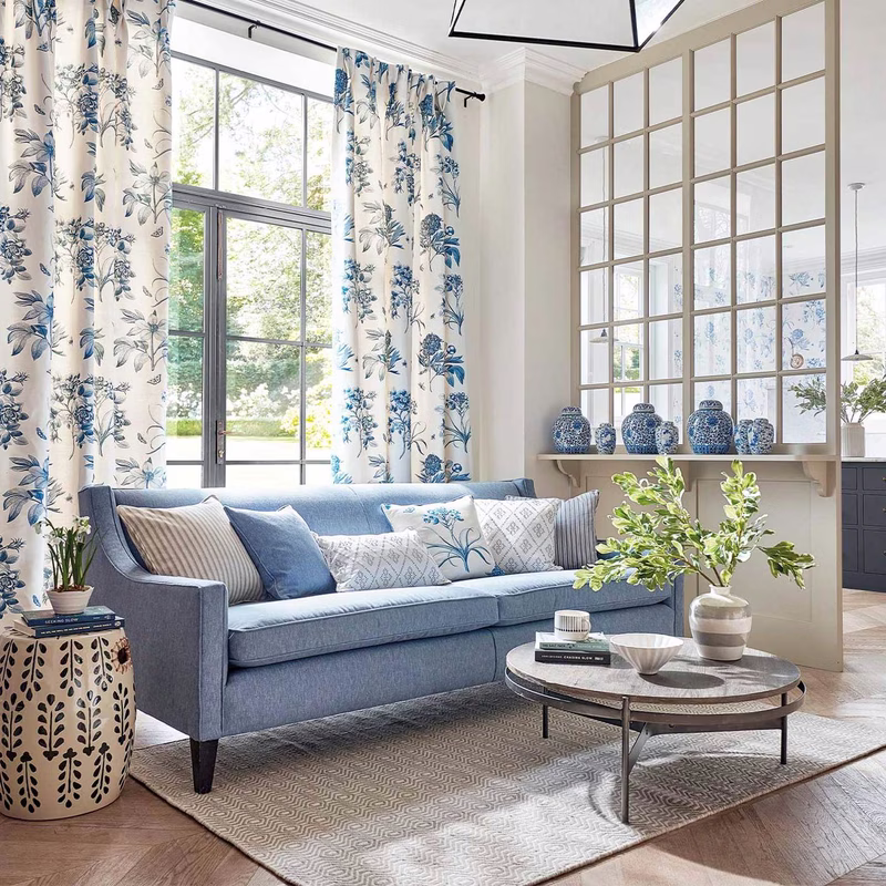 Bright living room with Etchings & Roses shown as floor-length curtains and cushions on a blue sofa.