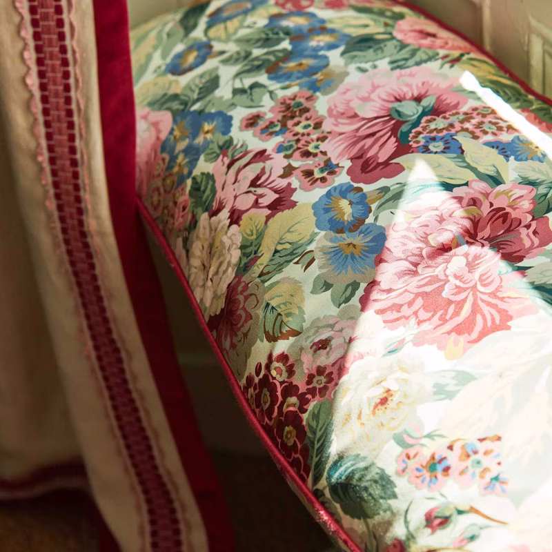 A close-up of a floral patterned upholstered seat or cushion with piped edging beside a red-trimmed curtain.